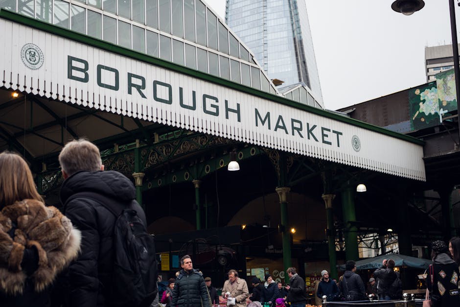 The image shows the entrance to Borough Market in Southwark, London, with a prominent white sign reading 'Borough Market' in bold black letters hanging beneath a green-framed canopy. The market's stru